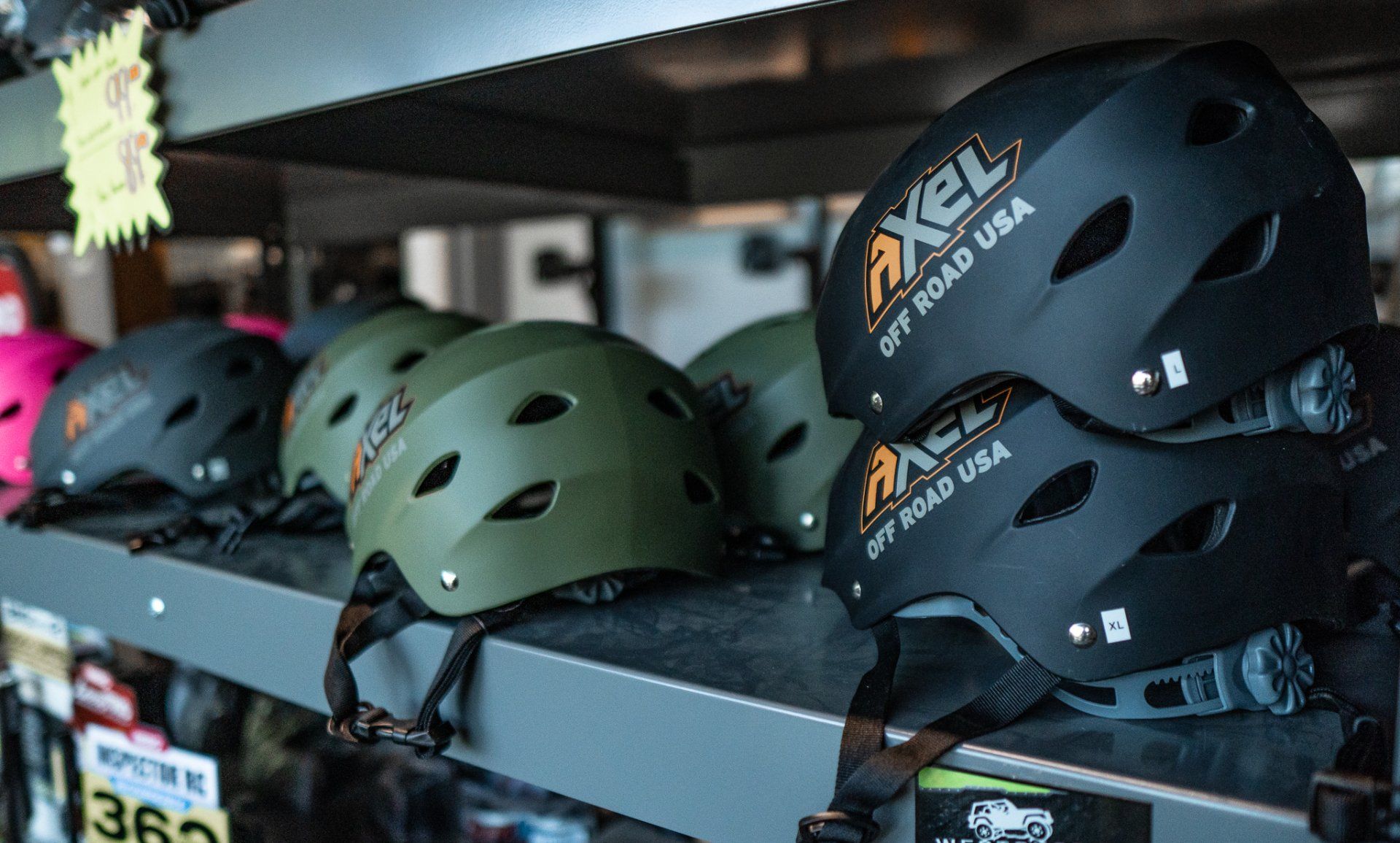 Helmets on a shelf for sale in a store; black, green, and pink colors.