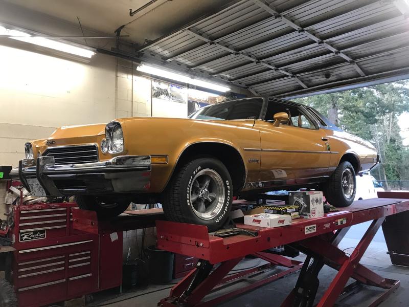 Gold classic car on a red lift in a garage.