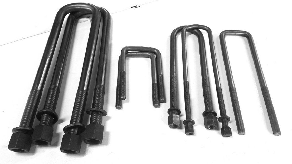 Various sizes of metal U-bolts with nuts and washers, arranged on a white surface.