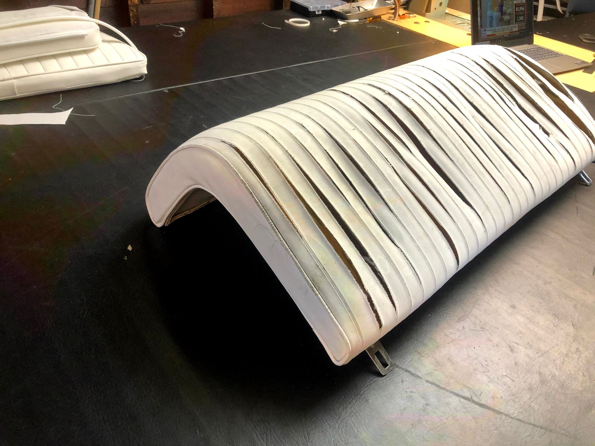 White, curved, upholstered bench on a black surface with strips of fabric attached.