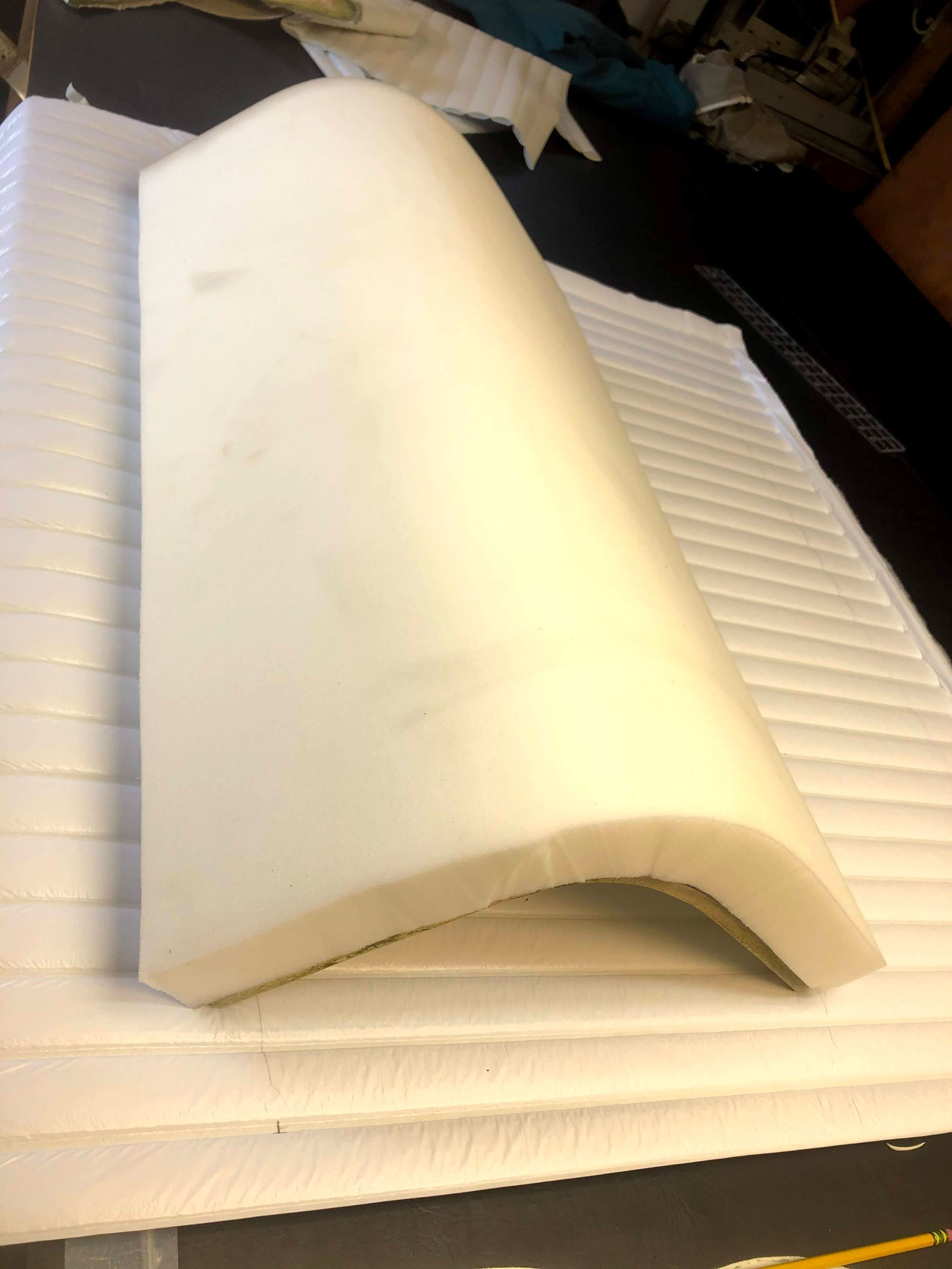 A white, curved foam cushion sits atop a stack of flat, white foam pieces, possibly for seating or padding.