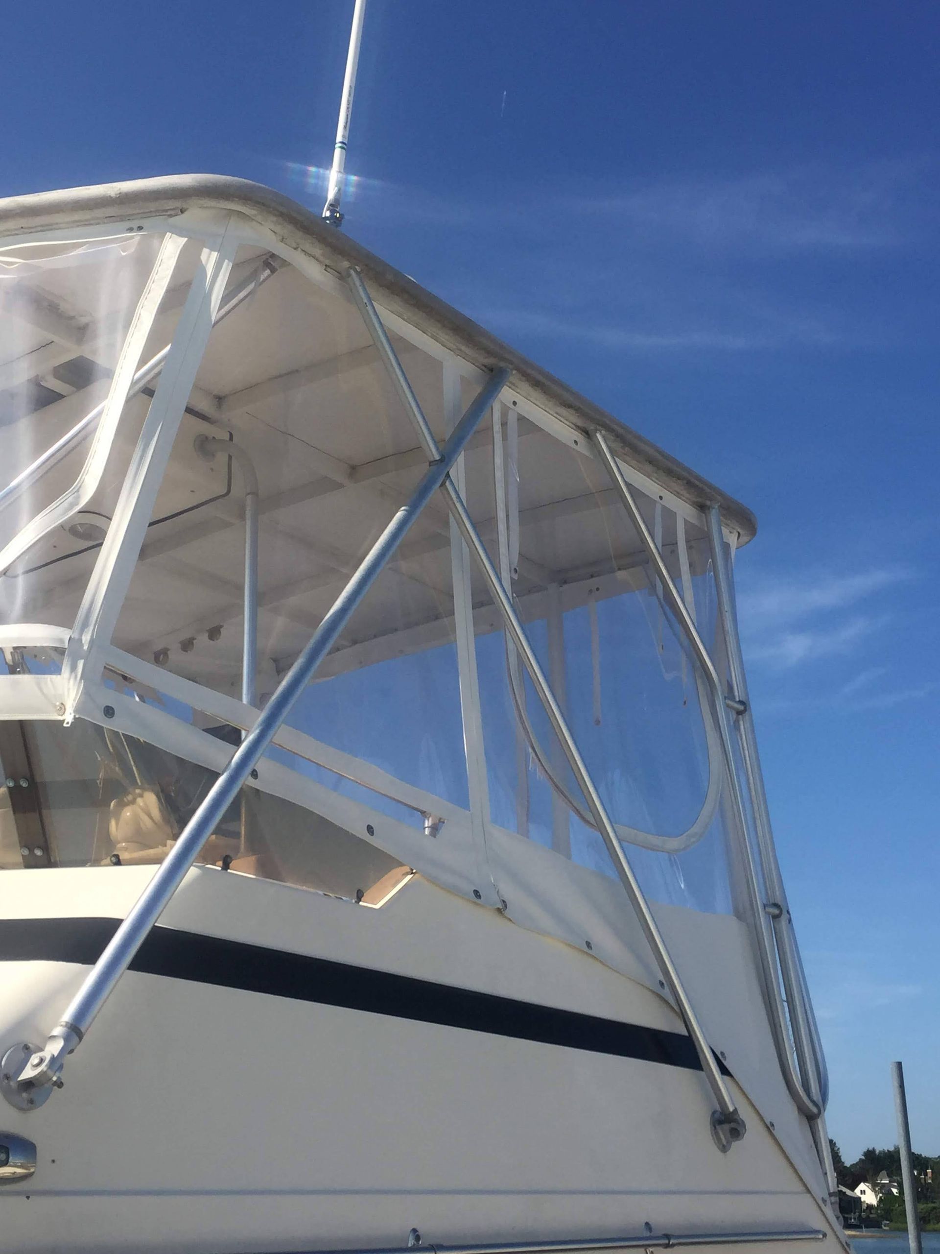 Boat cockpit with clear plastic enclosure, white frame, blue sky backdrop.