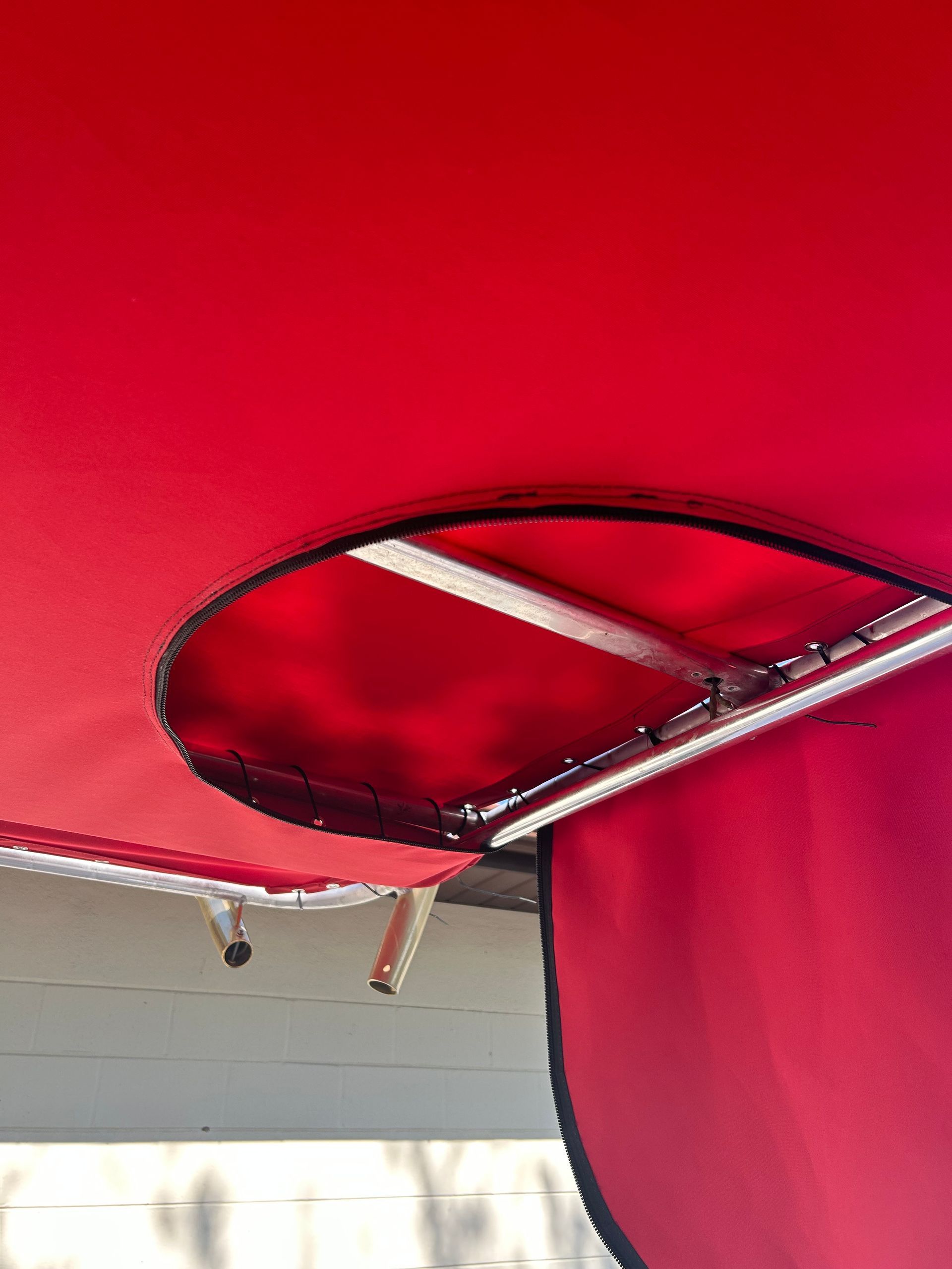 Red awning with an oval cut-out exposing a metal frame, with a red curtain hanging below.