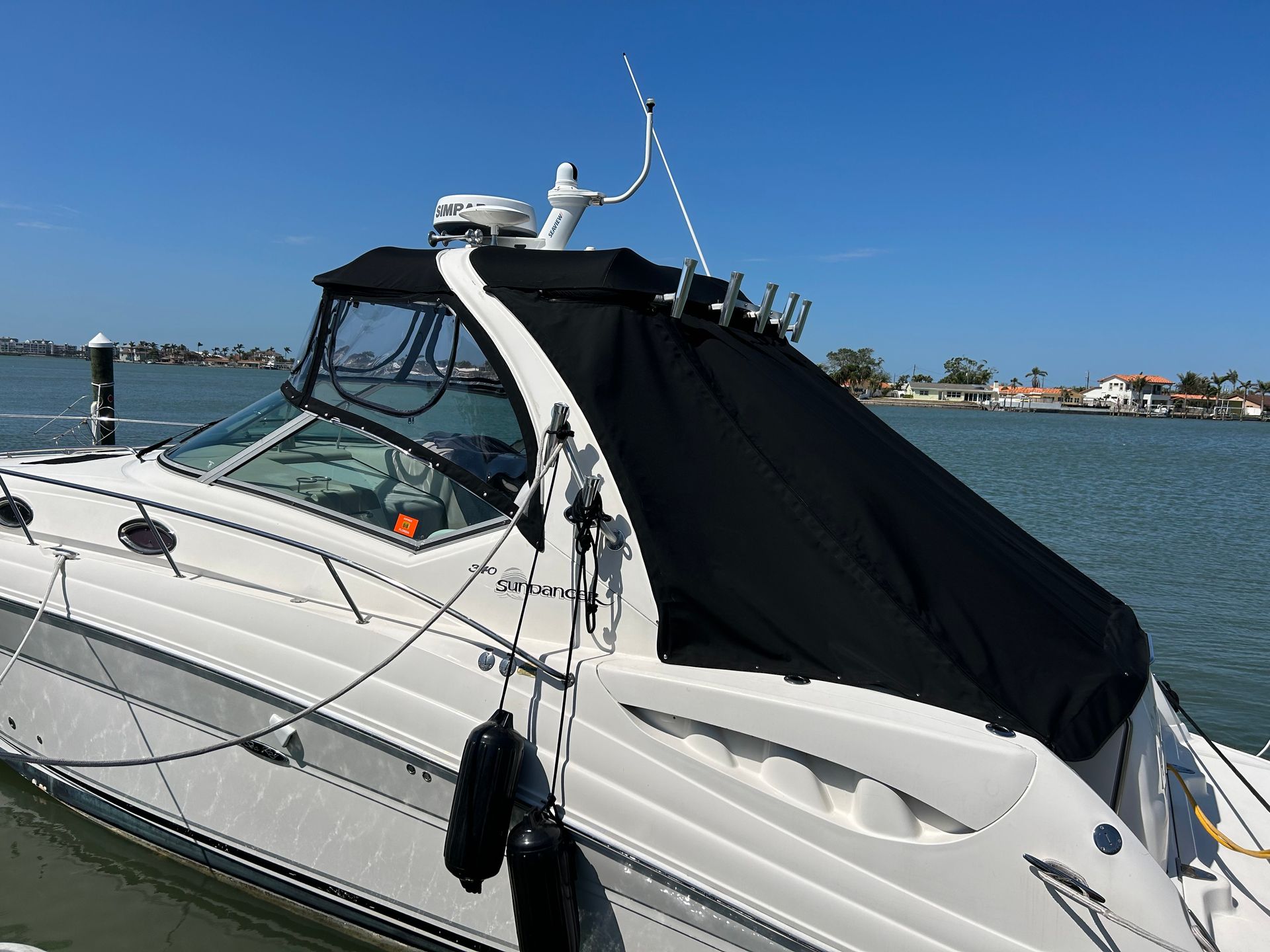 White motorboat with black canvas cover docked on a sunny day.