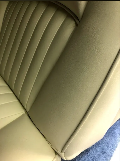 Cream-colored car seat with ribbed backrest and smooth side panel, close-up.