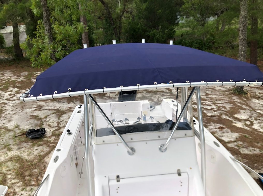 White boat with a dark blue and clear enclosure at a dock, with blue sky and clouds.