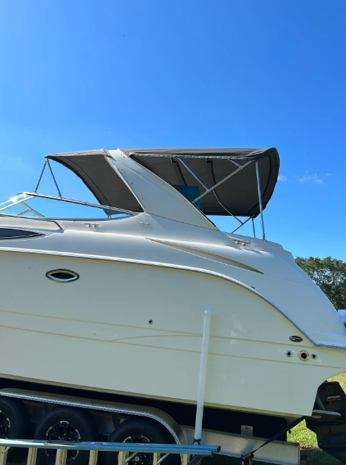 White motorboat on trailer, gray canvas top, blue sky.