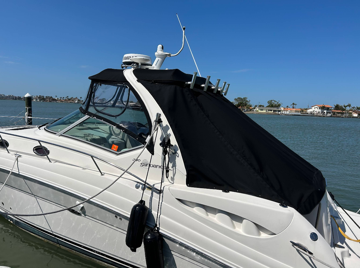 White boat with black canopy docked on a sunny day, blue water in the background.