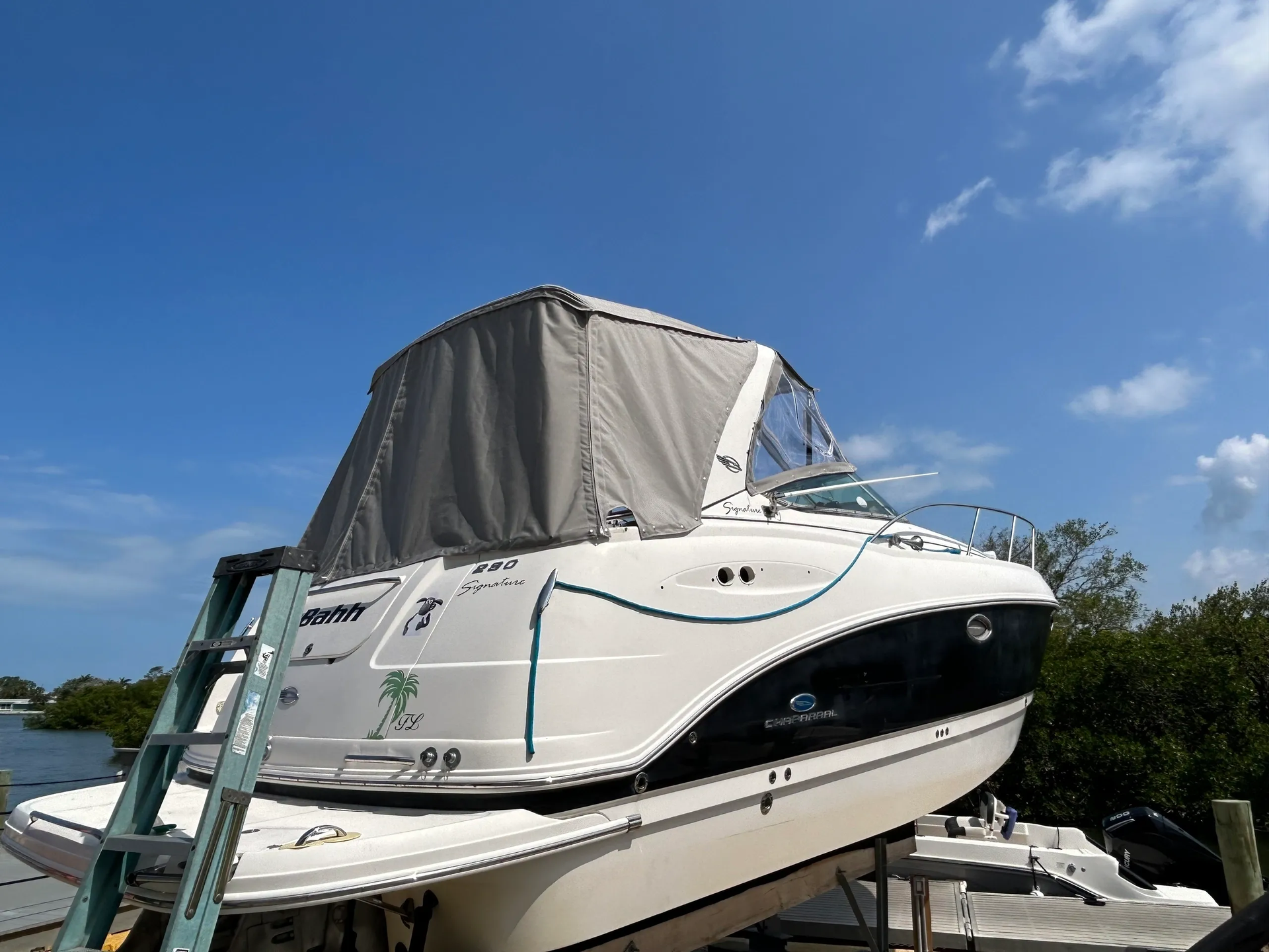 A white boat with a gray canopy on a lift. Blue sky.
