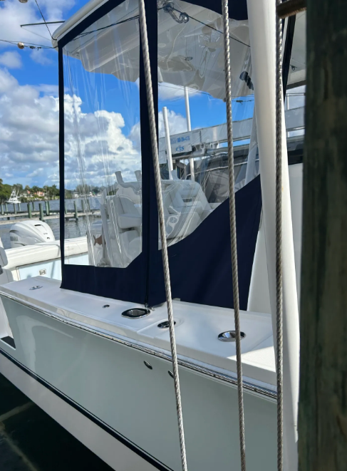 White boat with a dark blue and clear enclosure at a dock, with blue sky and clouds.