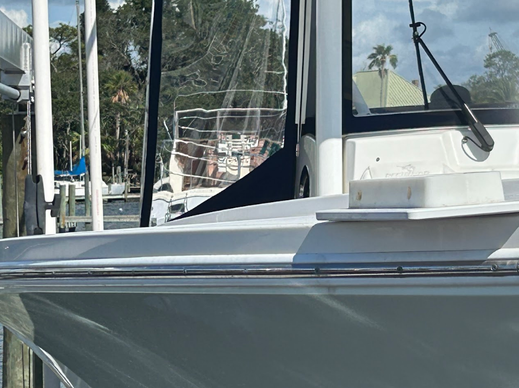 White boat with windshield and clear enclosure docked at a marina.