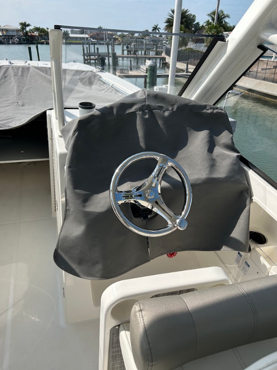 Boat steering wheel covered by a gray cover, docked near a marina.