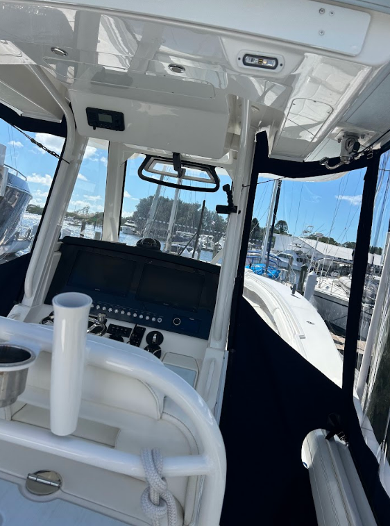 Interior view of a boat's helm station with a console, windshield, and surrounding windows.