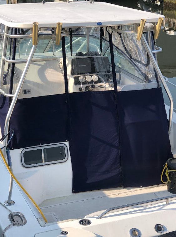 A boat's cockpit with navy blue canvas enclosure and clear vinyl windows; white frame, sunny setting.