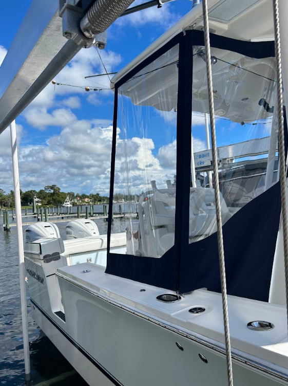 White boat with blue and clear enclosure, docked near a marina.