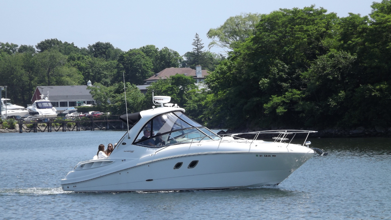 White motorboat cruising on water near trees and buildings.