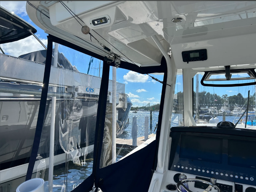 Inside boat cabin with clear vinyl enclosure, dock, water, and other boats visible.