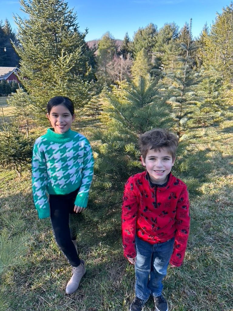 A boy and a girl are standing next to each other in front of a christmas tree.
