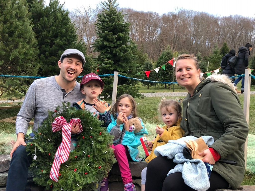 A family is sitting on a bench at a christmas tree farm holding a wreath.