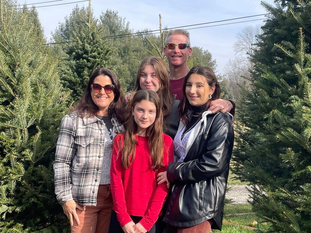 A family is posing for a picture in front of a christmas tree farm.