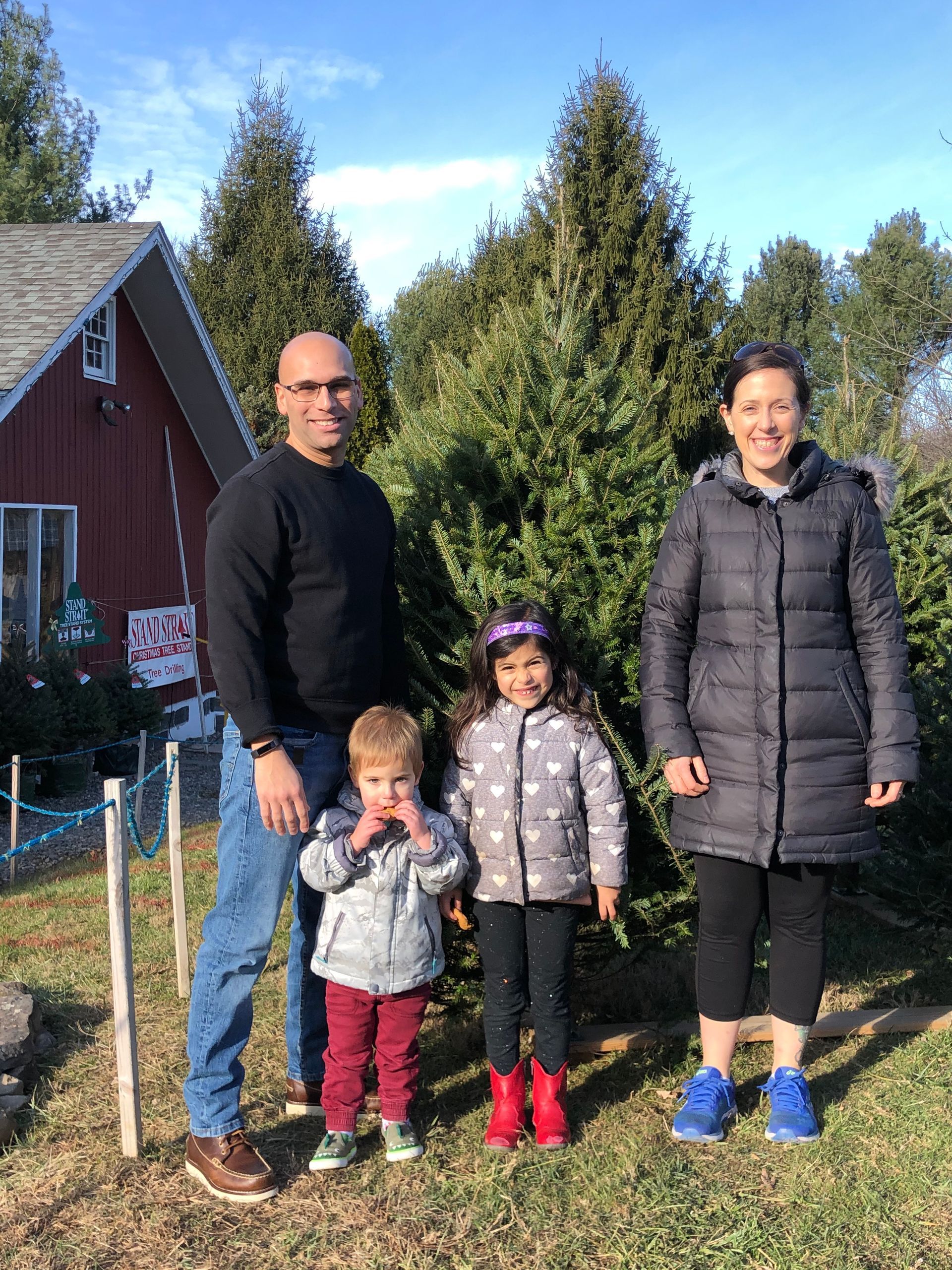 A family is standing in front of a christmas tree farm.