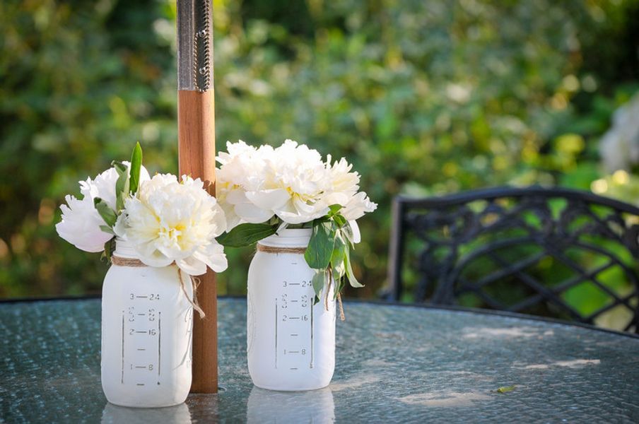 Two white mason jars filled with white flowers are sitting on a table