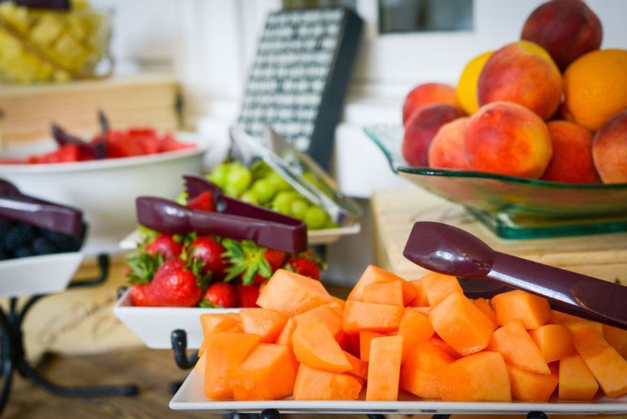 A buffet table with plates of fruit and tongs on it