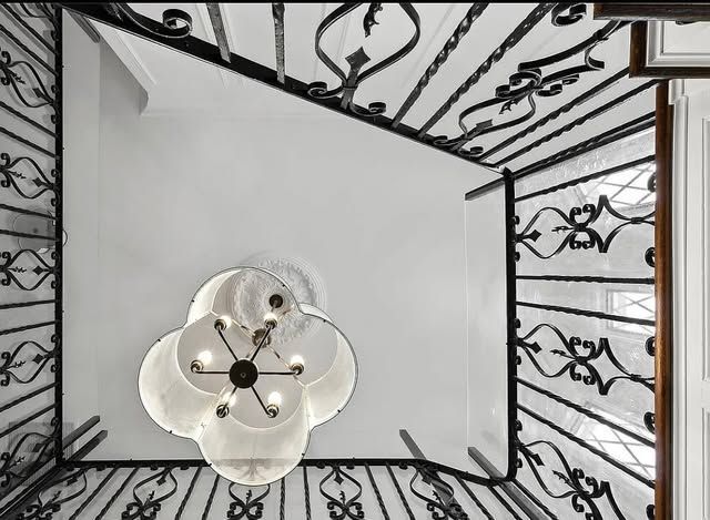A black and white photo of a staircase with a chandelier hanging from the ceiling.