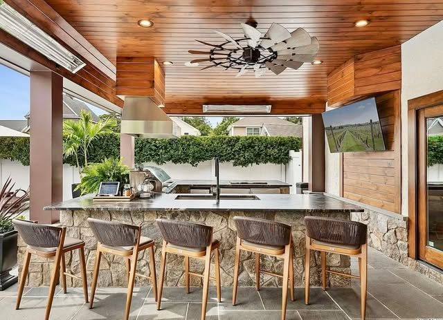 A large outdoor kitchen with a ceiling fan and stools.