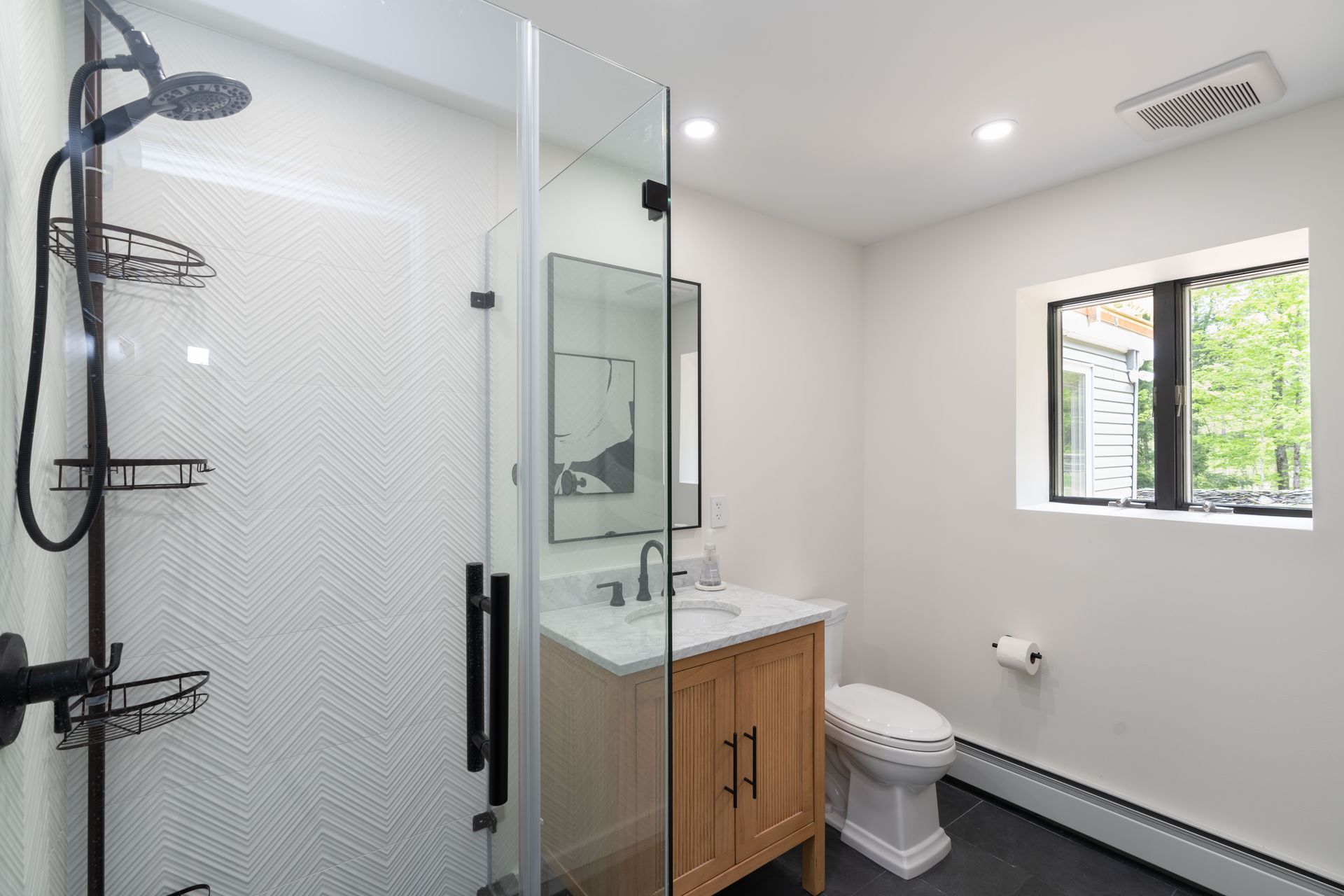 A bathroom with a toilet , sink , shower and window.
