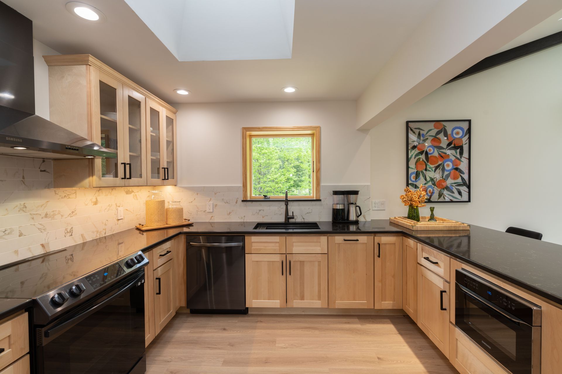 A kitchen with wooden cabinets , black counter tops , stainless steel appliances and a window.