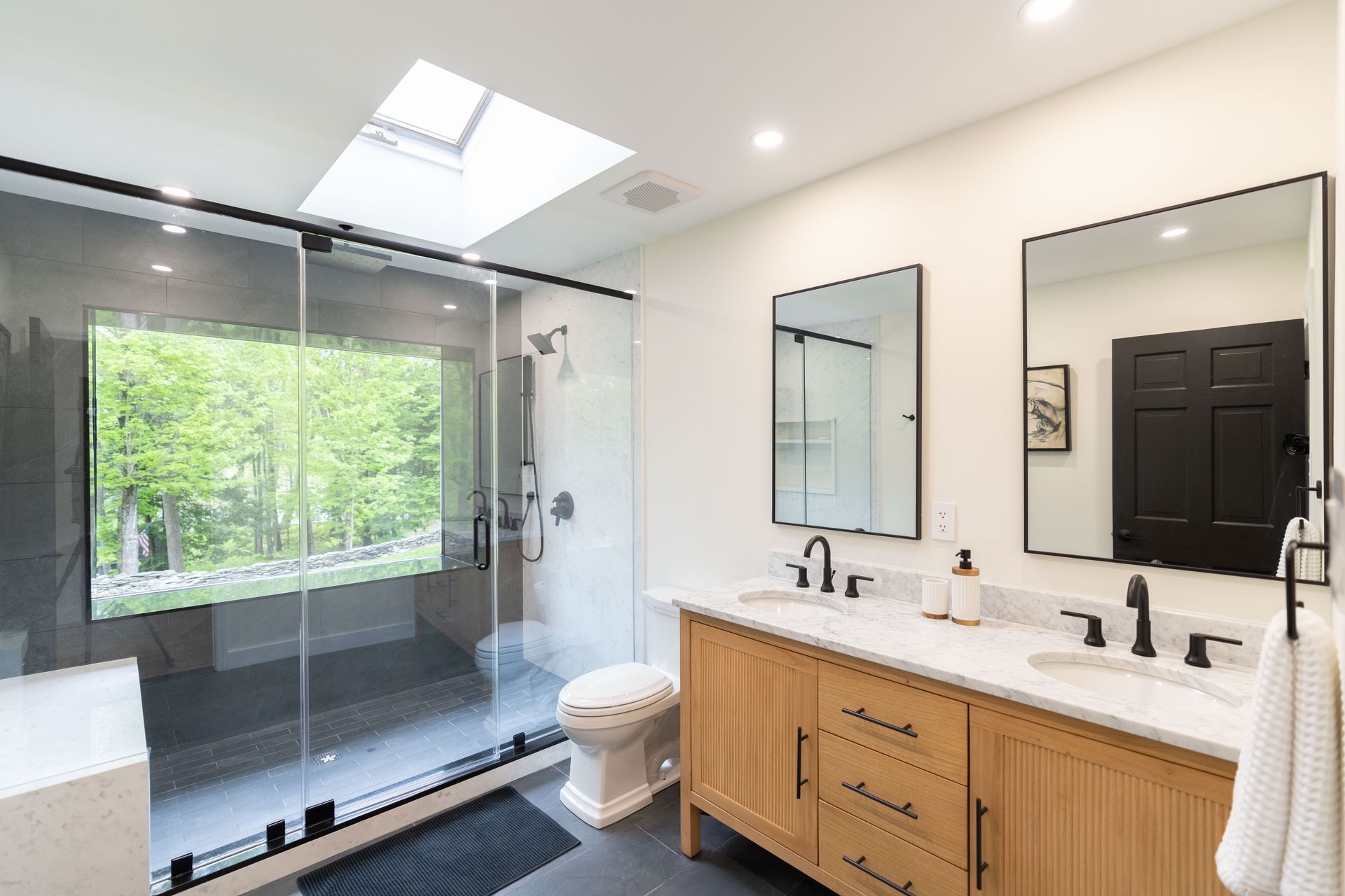 A bathroom with two sinks , a toilet , a walk in shower and a skylight.