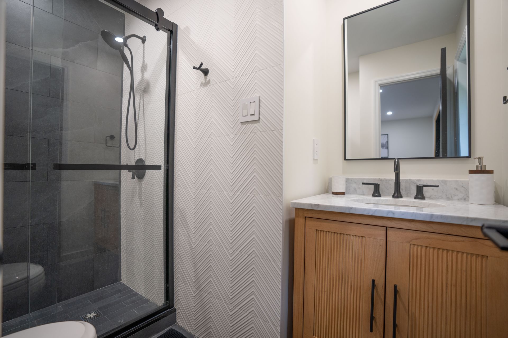 A bathroom with a walk in shower , sink , mirror and toilet.