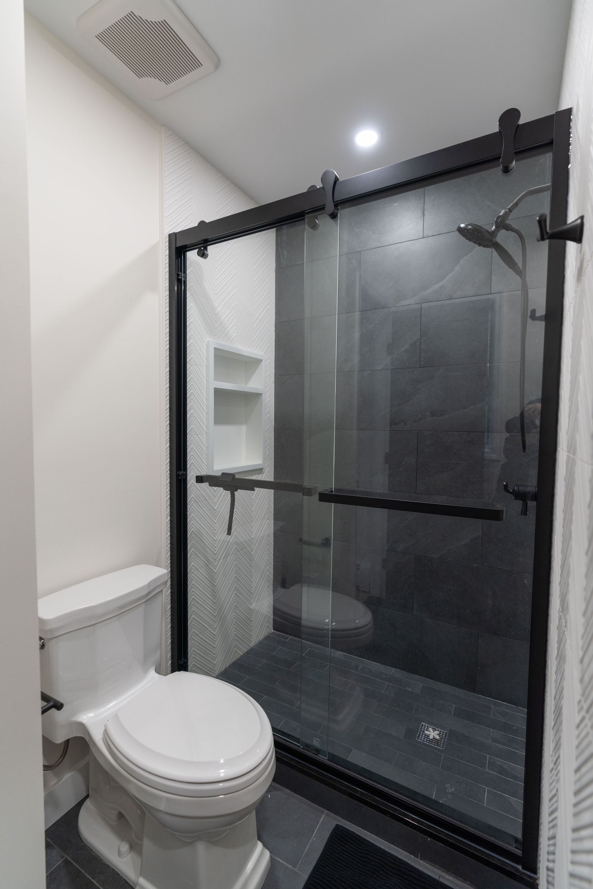A bathroom with a toilet , shower and sliding glass door.