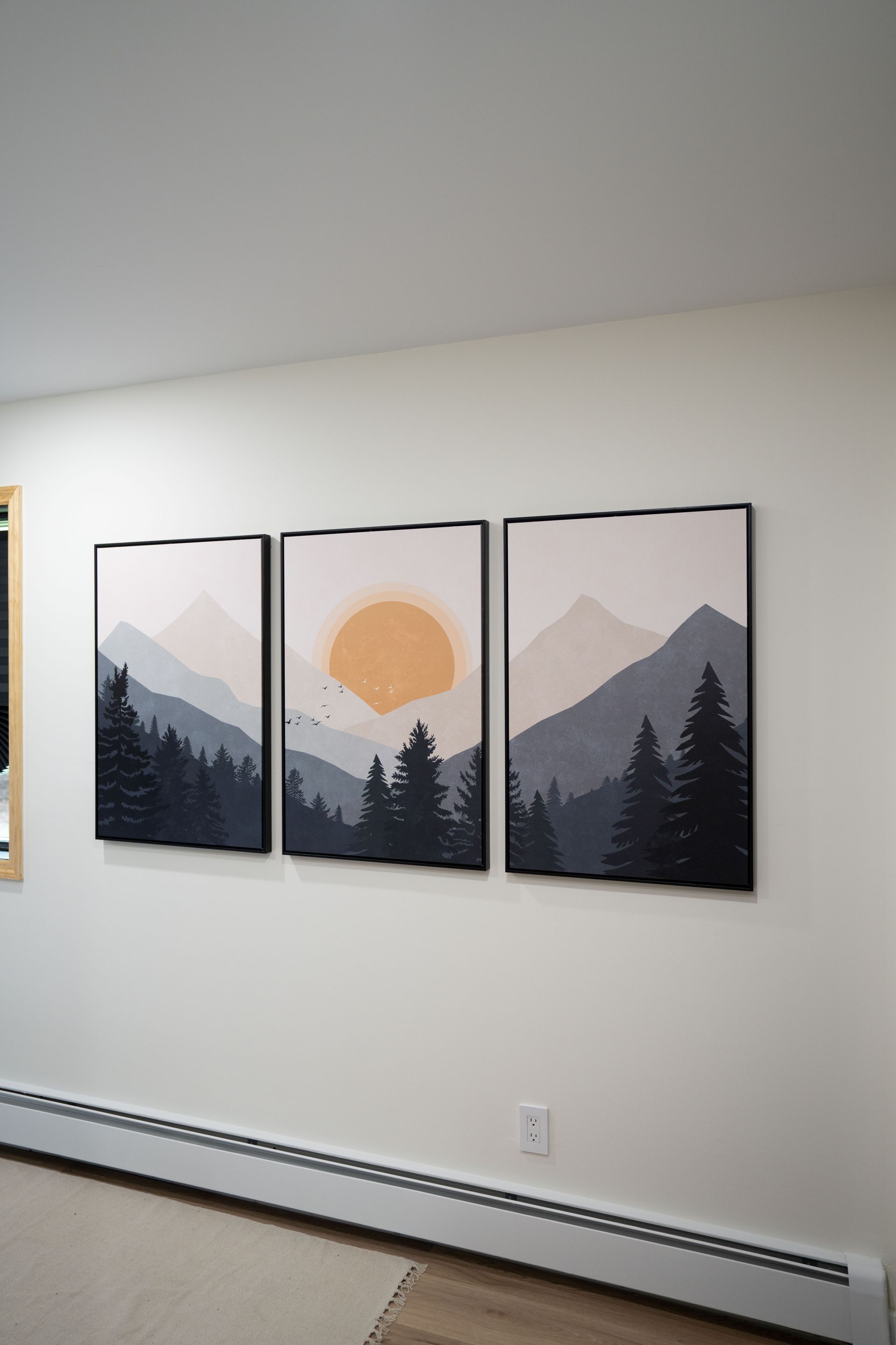 Three paintings of mountains and trees are hanging on a wall.