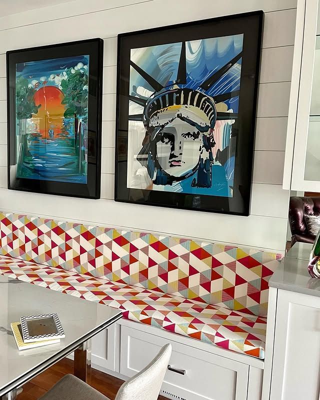 Two paintings of the statue of liberty are hanging on a wall above a bench.