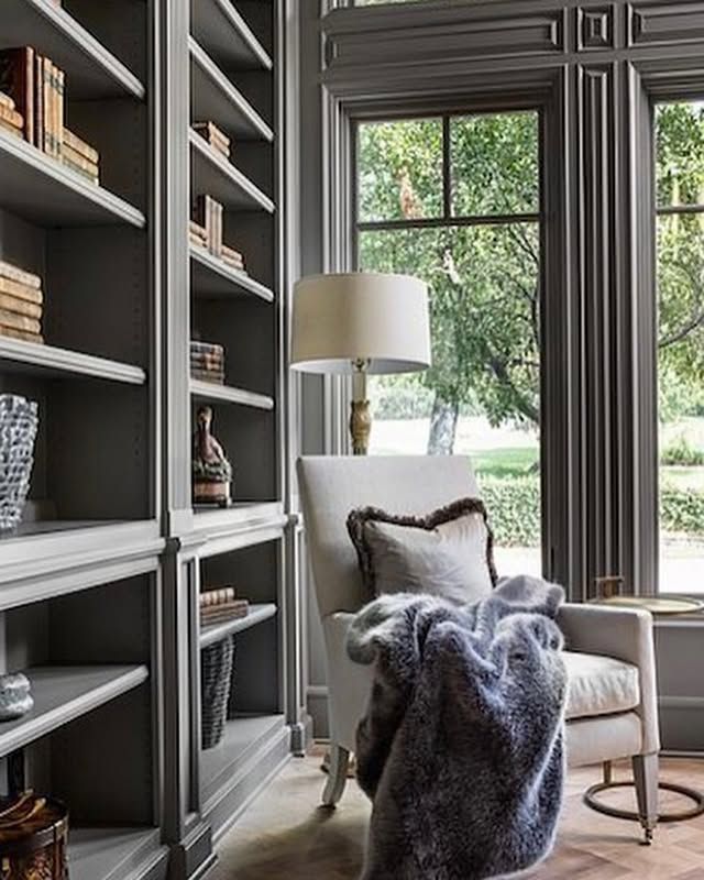 A living room with a chair , bookshelf , lamp and window.