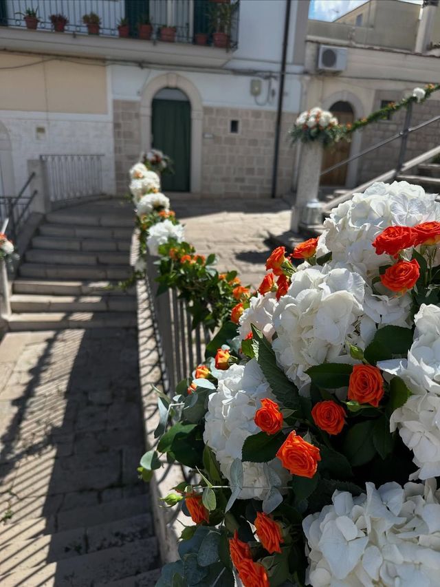 Un vialetto fiorito conduce all'ingresso di un edificio in pietra con scale e piante in vaso.