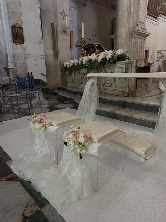 Altare nuziale con composizioni floreali bianche e drappeggi di tessuto all'interno di una chiesa.