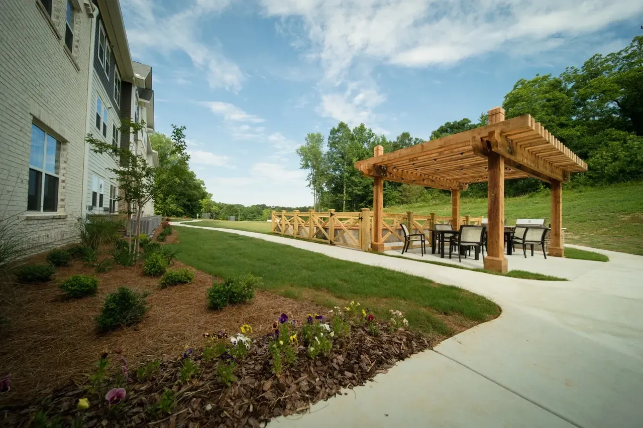 Outdoor community space with a wooden pergola and seating near landscaped lawn.