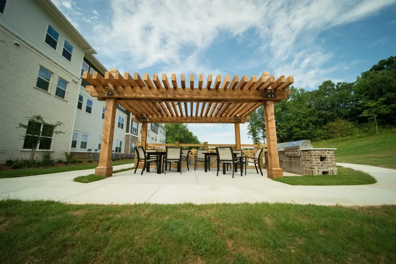 Communal outdoor seating area under a wooden pergola beside an apartment building.