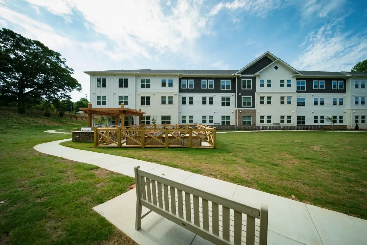 Exterior view of a modern apartment building with a landscaped lawn, walkway, and benches.