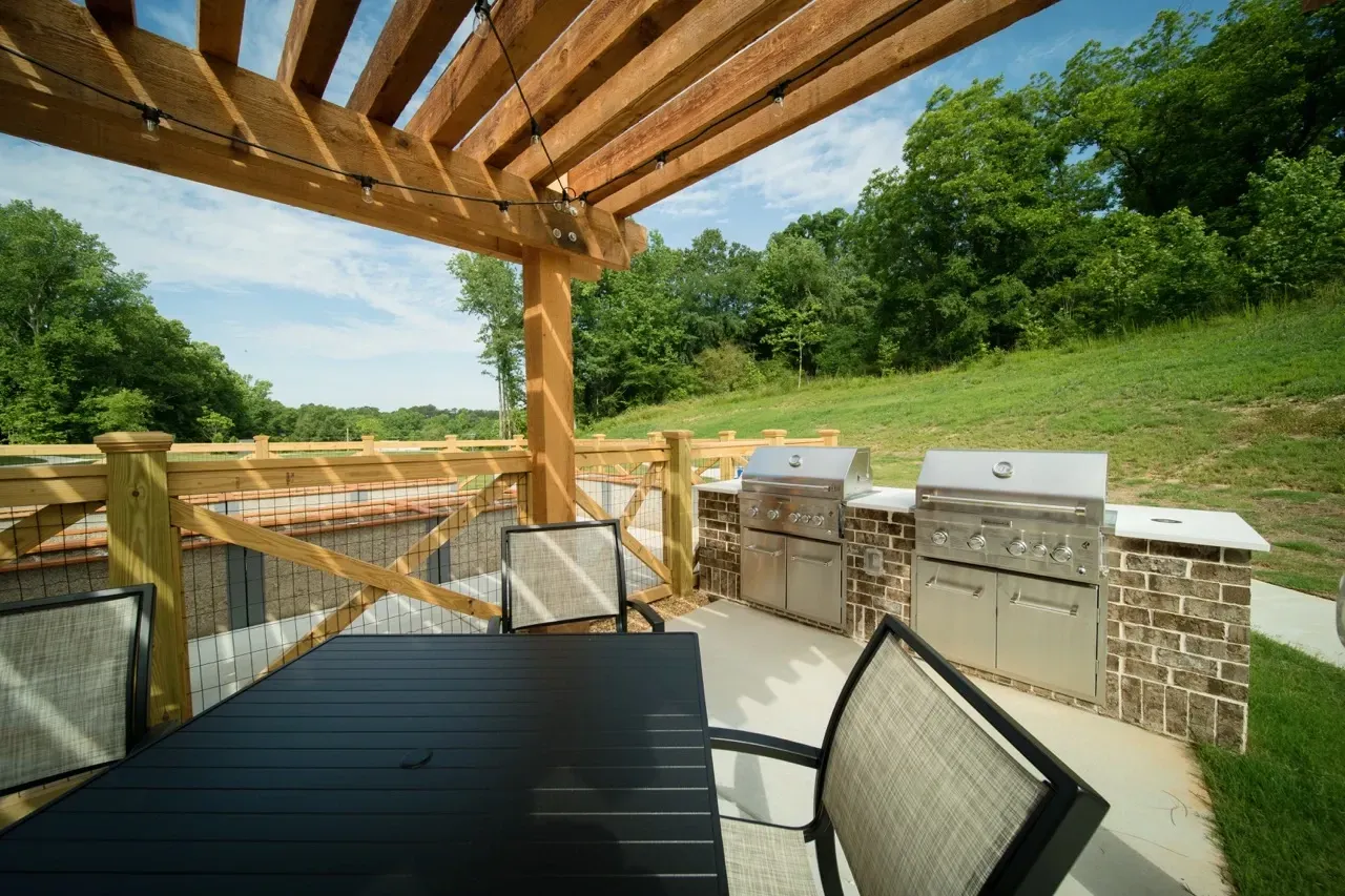 Outdoor communal grilling area under a wooden pergola with string lights and stainless steel grills.
