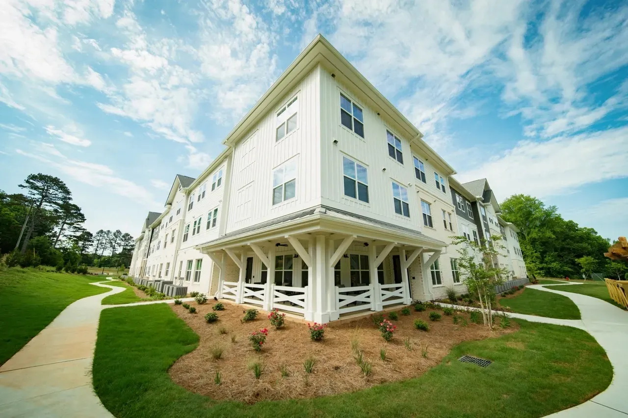 Exterior view of a white multi-story apartment building with a covered ground-floor entry and curved sidewalks.