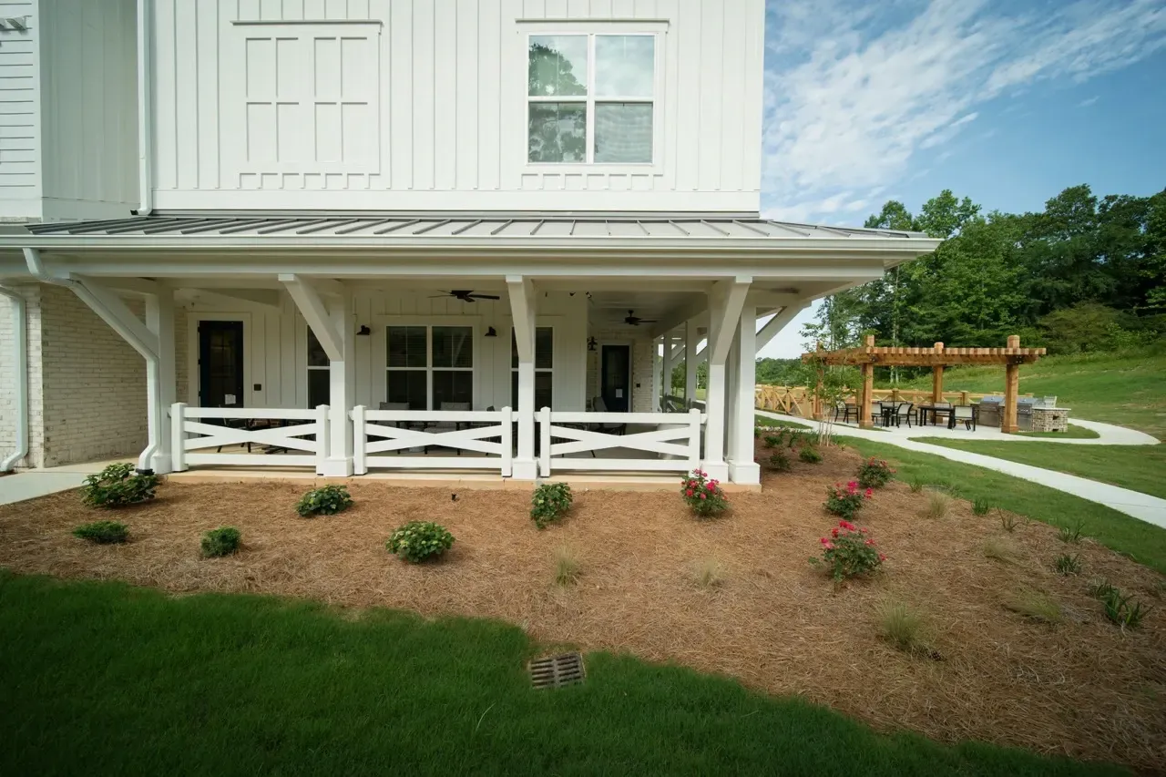 White two-story building with a covered porch, crisscross white fencing, and a wooden pergola with outdoor seating.