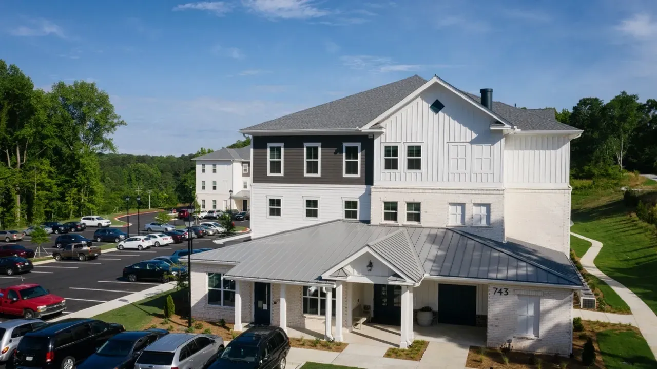 Exterior view of a multi-story apartment building with a covered entrance and adjacent parking.