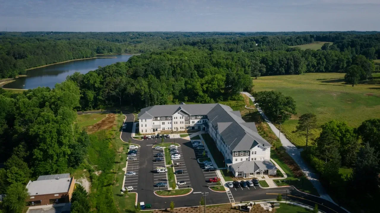 Aerial view of a multifamily apartment complex surrounded by trees and a lake.