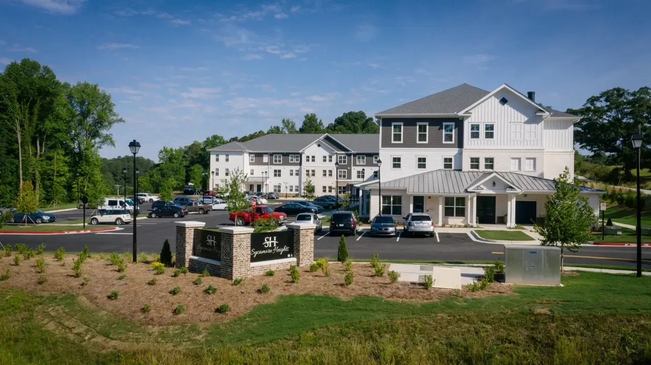 Exterior view of Sycamore Heights apartment community with signage, parking, and multiple buildings.