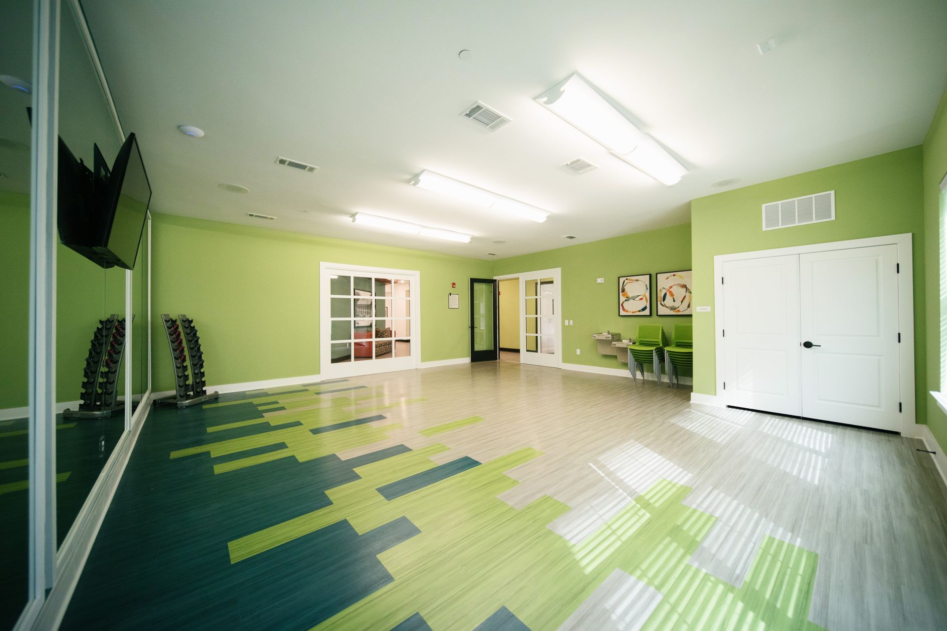 Bright meeting room with rows of blue and beige chairs, wall mirror, ceiling fans, and large windows