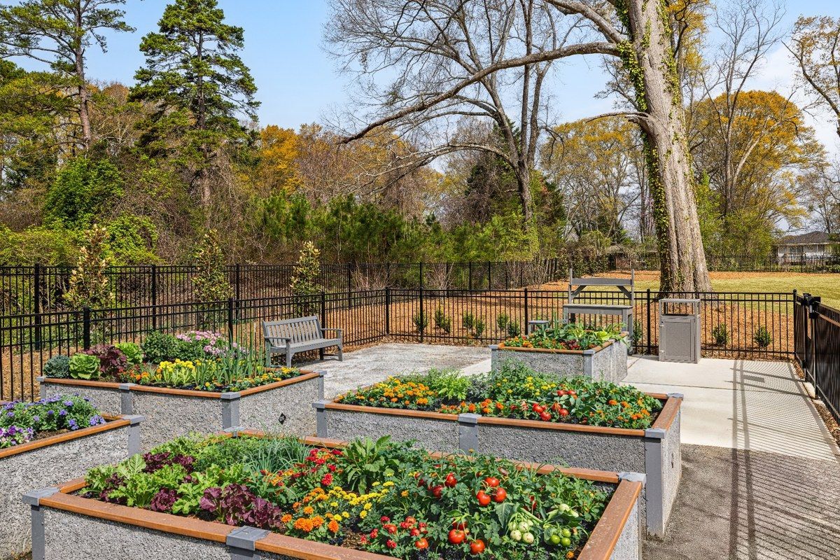 Raised flower beds in a landscaped garden with colorful blooms, gravel paths, and trees beyond.